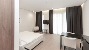 A modern hotel room with a bed, a desk, a chair, and a TV.