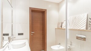 A modern bathroom with a wooden door, a round sink, a smaller sink, and a large mirror.
