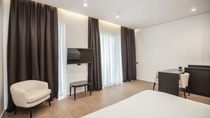 A modern hotel room with a large bed, a TV mounted on the wall, a small table, and a chair.