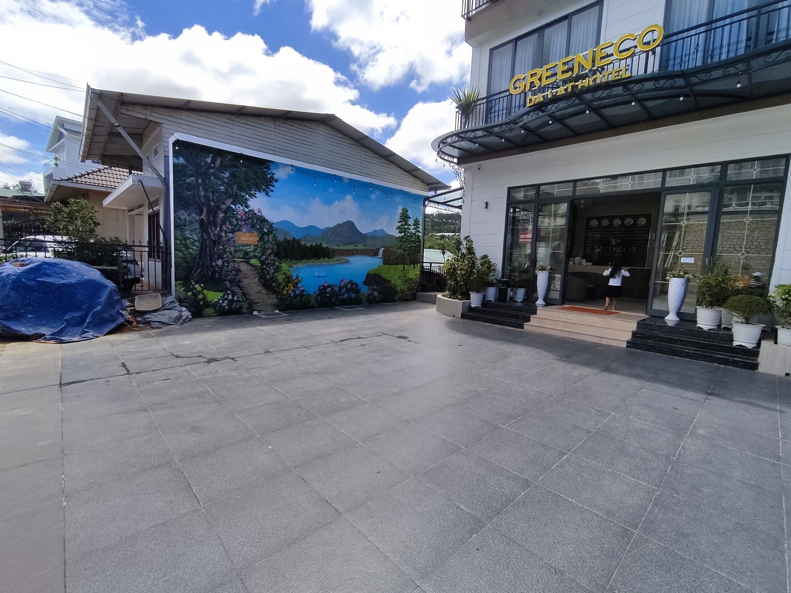Ein Hotel mit Eingangsbereich, einer Wandmalerei einer schönen Landschaft, einem überdachten Außenbereich und einem gepflegten Garten.
