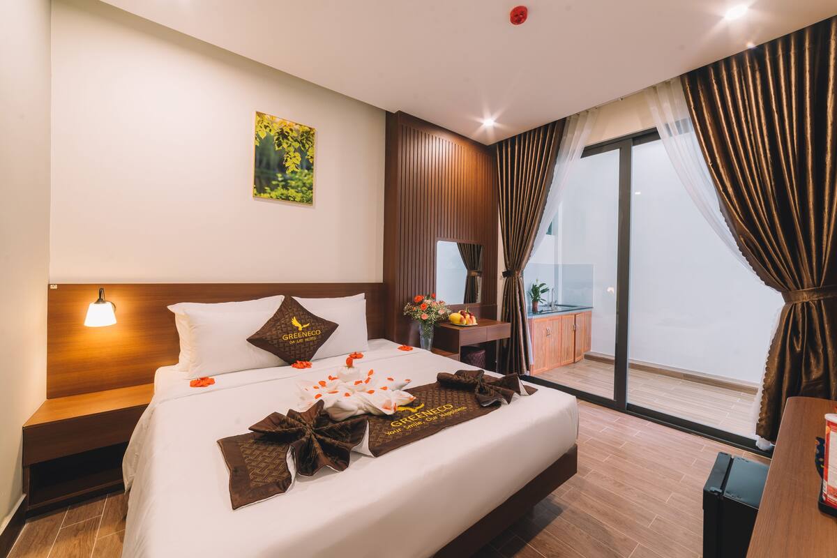 A hotel room with a bed, a nightstand, a desk, a chair, a window with curtains, and a view of the outside.