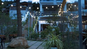 A modern building with a glass facade, outdoor seating, and string lights. - Green Eco Hotel Dalat (Xuan Huong - Da Lat)