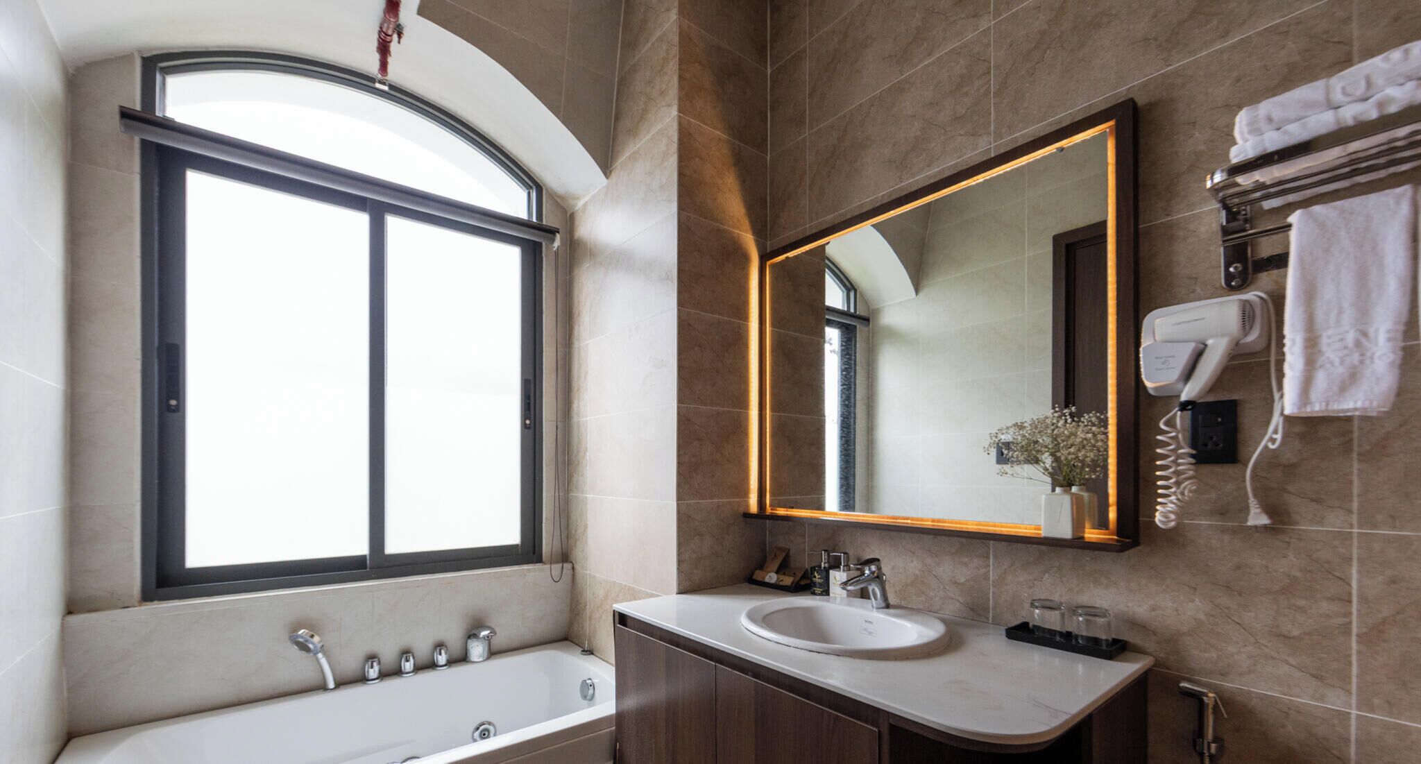 Un baño moderno con bañera, lavamanos, un espejo grande y una ventana.