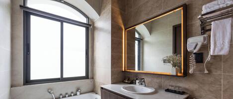 Un baño moderno con bañera, lavamanos, un espejo grande y una ventana.