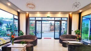 A modern lobby with plush seating, a chandelier, and large windows offering a view of the street and greenery outside. - Green Eco Hotel Dalat (Xuan Huong - Da Lat)
