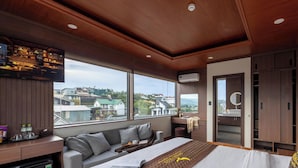 A modern hotel room with a large bed, a seating area, a minibar, and a view of the city. - Green Eco Hotel Dalat (Xuan Huong - Da Lat)