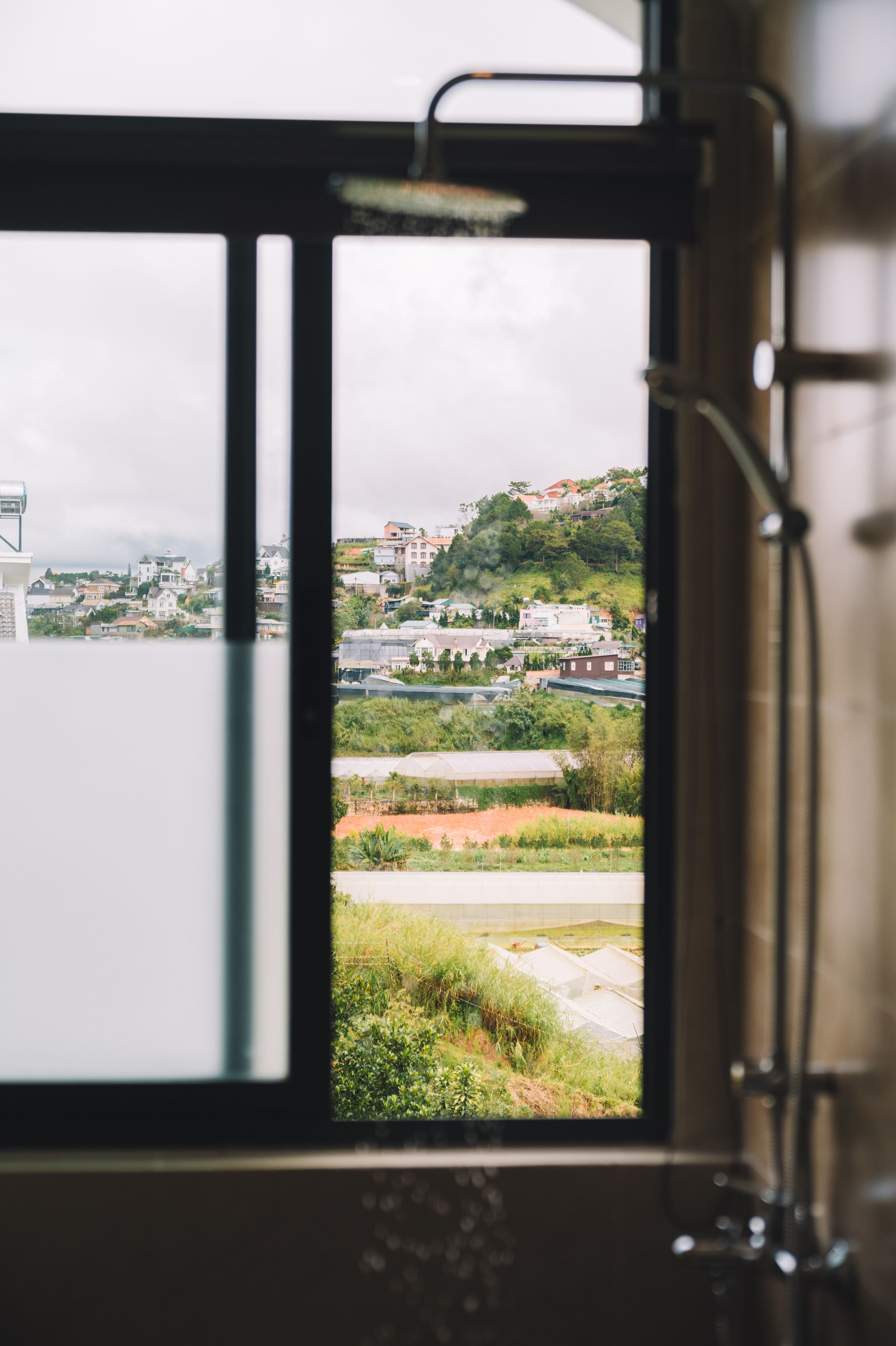 A window view of a residential area with houses, greenery, and a distant hill.