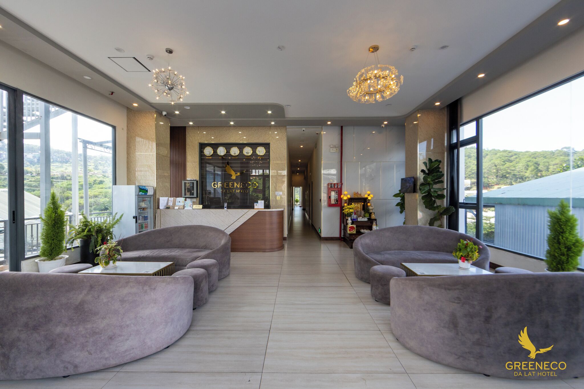 Un hall d’hôtel moderne, doté d’un comptoir d’accueil, de fauteuils confortables, de grandes fenêtres et d’un lustre.