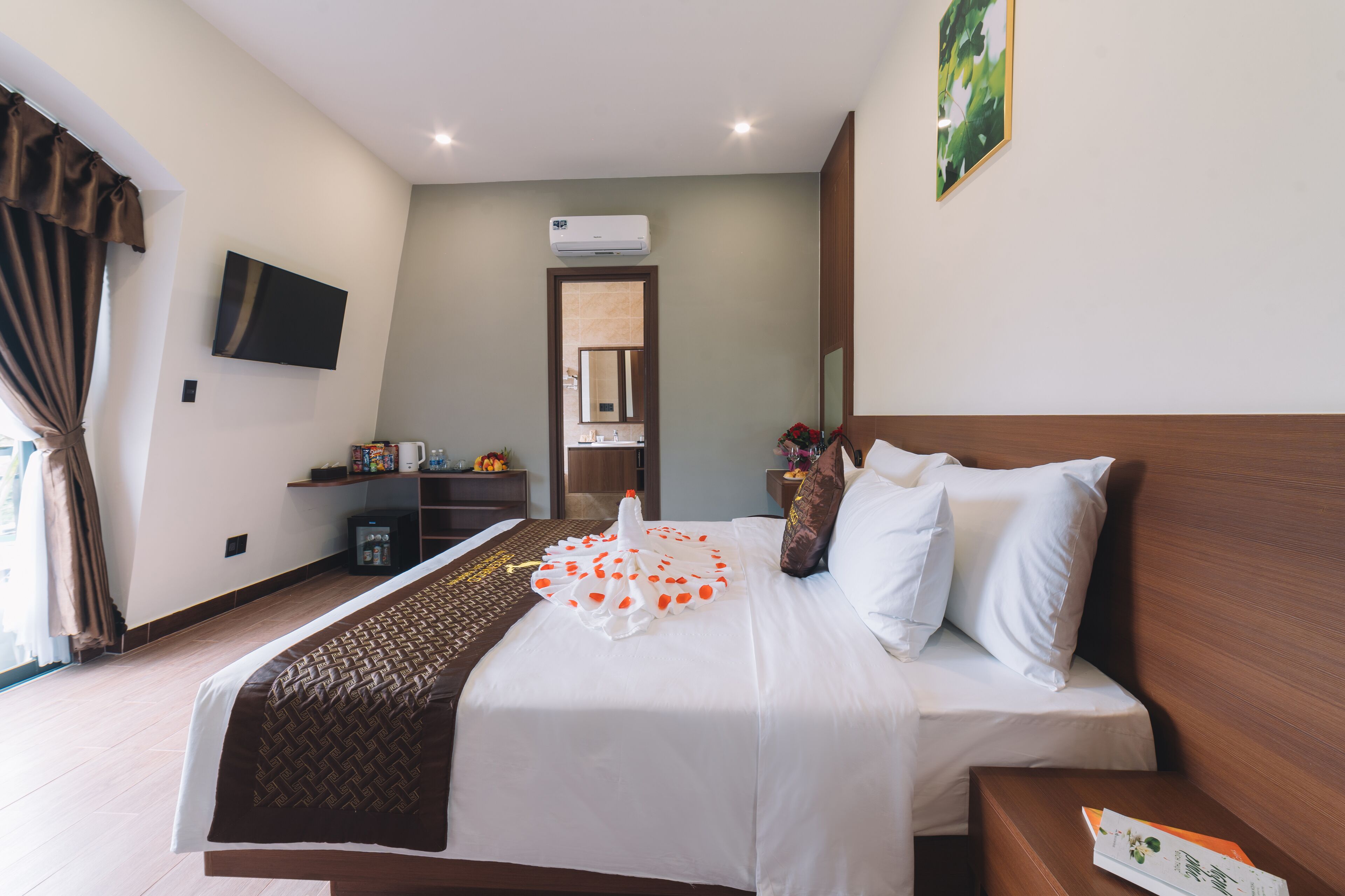 A hotel room with a large bed, a flat-screen TV mounted on the wall, a small desk with a chair, and a bathroom visible through an open door.
