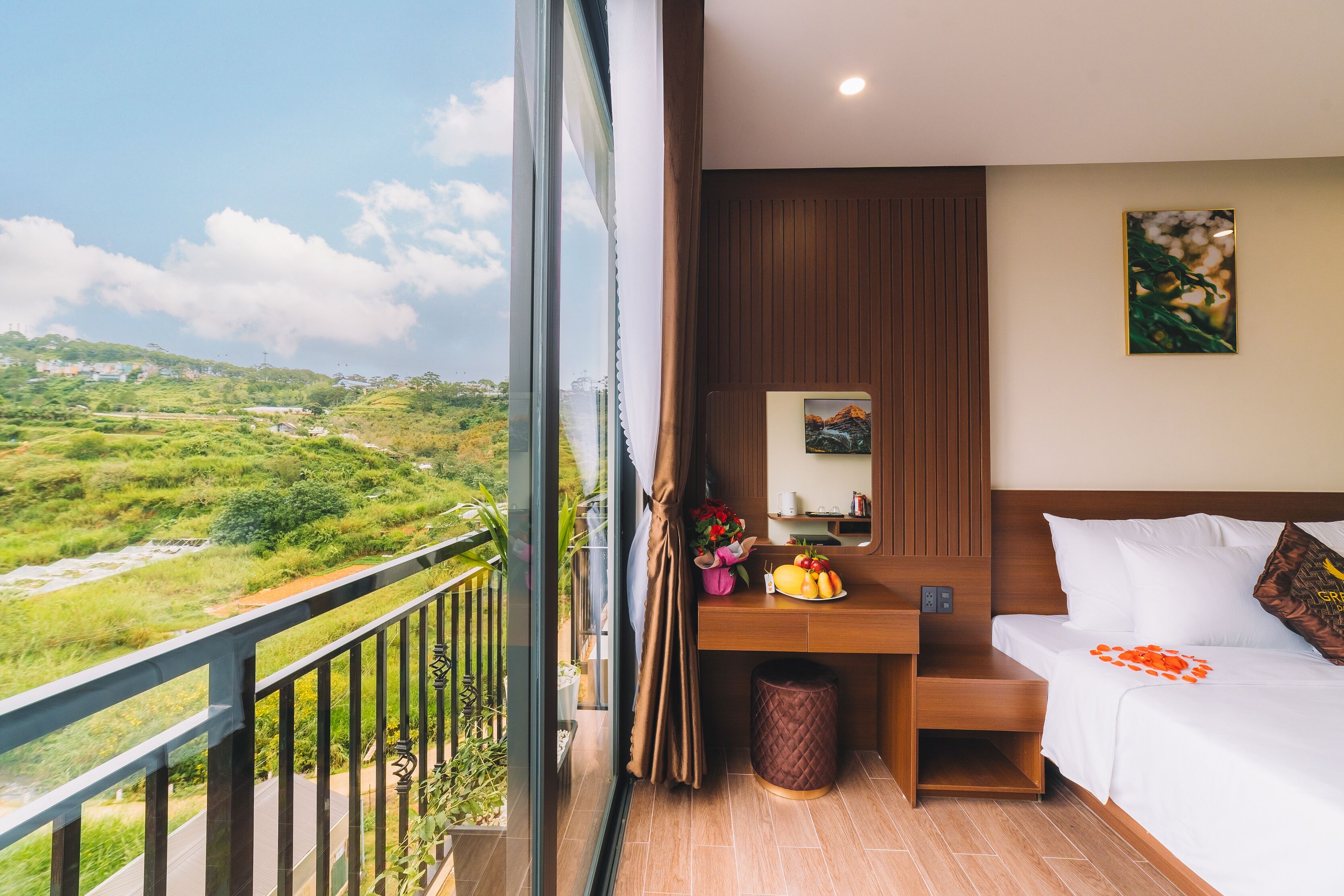 Une chambre d’hôtel avec un balcon, un lit, un bureau agrémenté d’un vase de fleurs et une vue sur un paysage verdoyant.