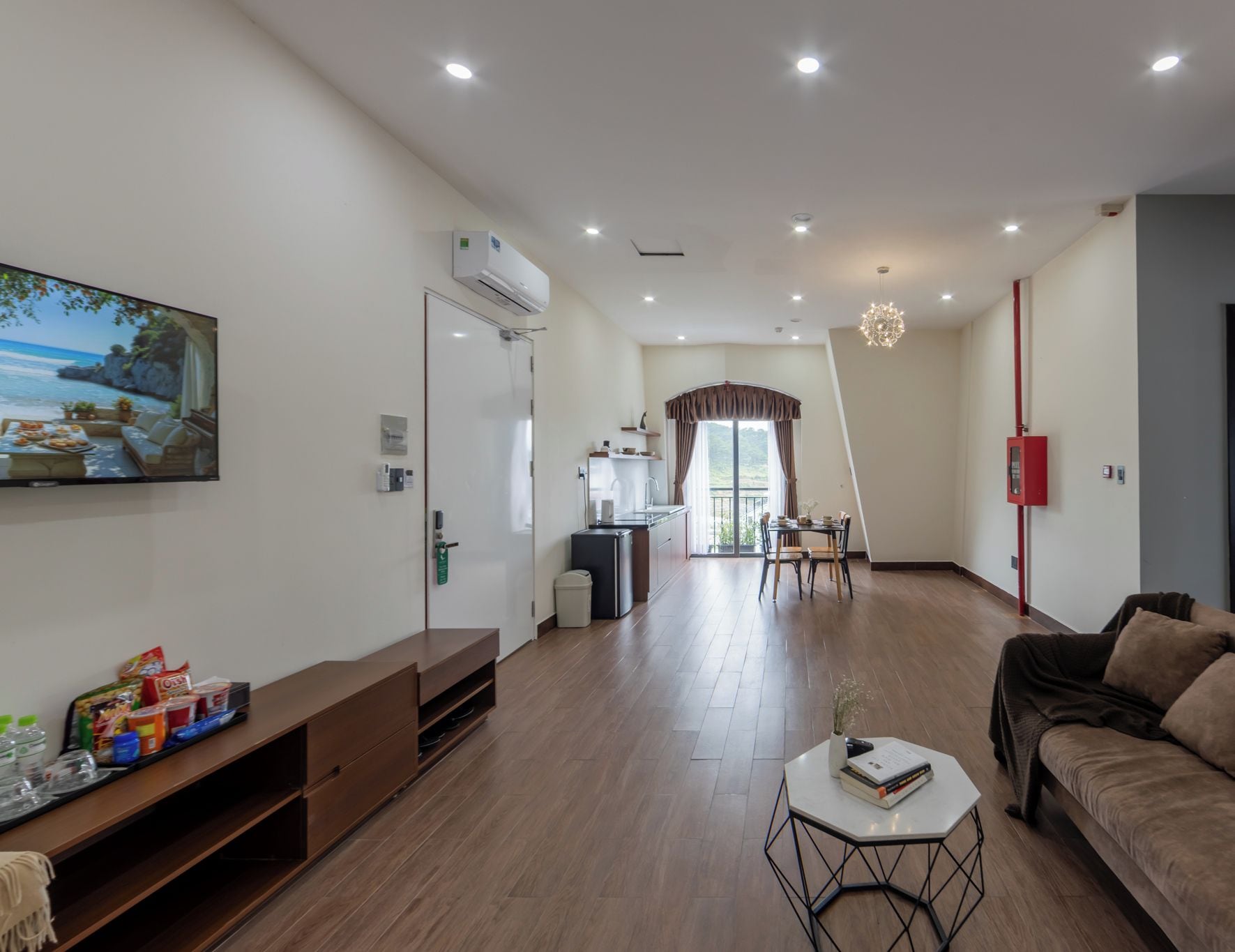 A modern hotel room with a living area, a dining table, and a kitchen in the background.