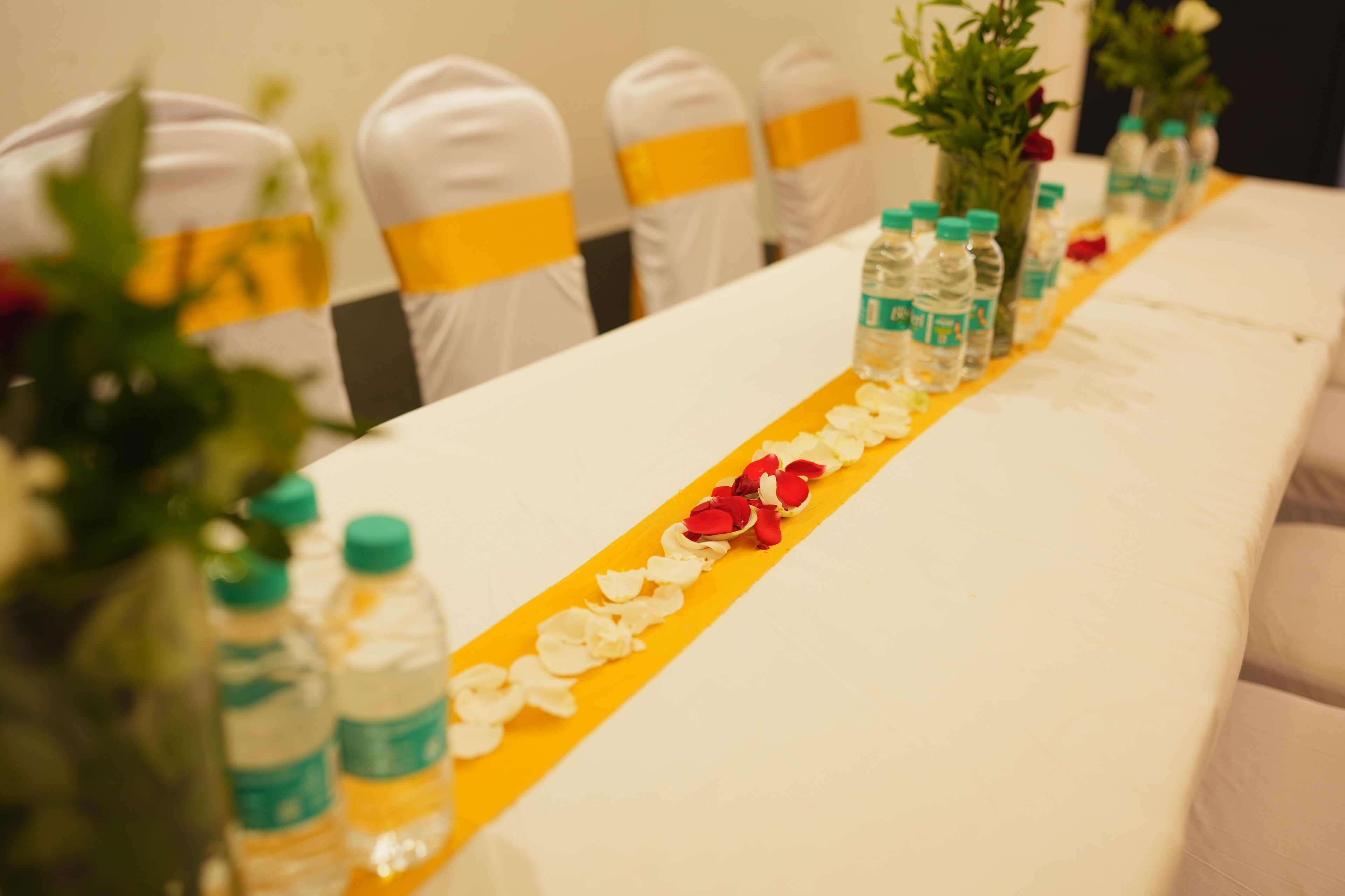 A conference table with water bottles, flower petals, and a yellow runner.