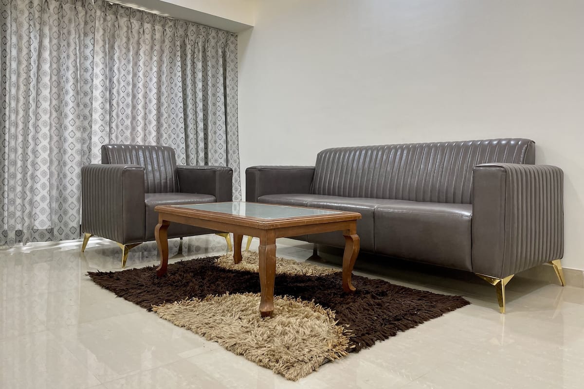 Un salon avec un canapé gris, deux fauteuils, une table basse en verre et un rideau à motifs.
