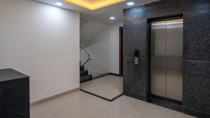 A modern elevator with a control panel, a staircase leading to another floor, and a recessed ceiling light.