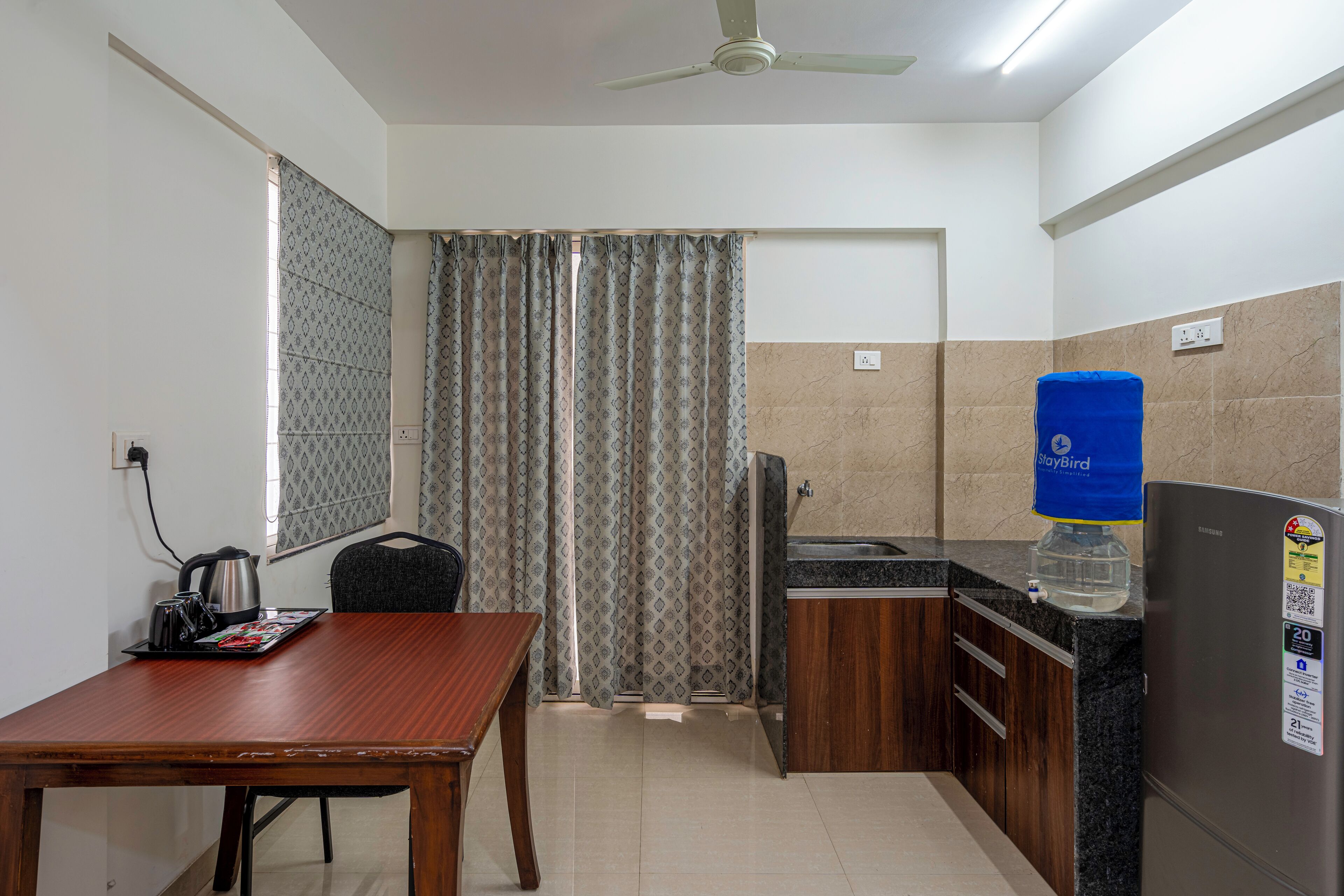 A compact kitchen with a dining table, a refrigerator, a water dispenser, and a kettle.