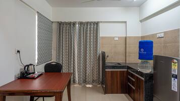 A compact kitchen with a dining table, a refrigerator, a water dispenser, and a kettle.
