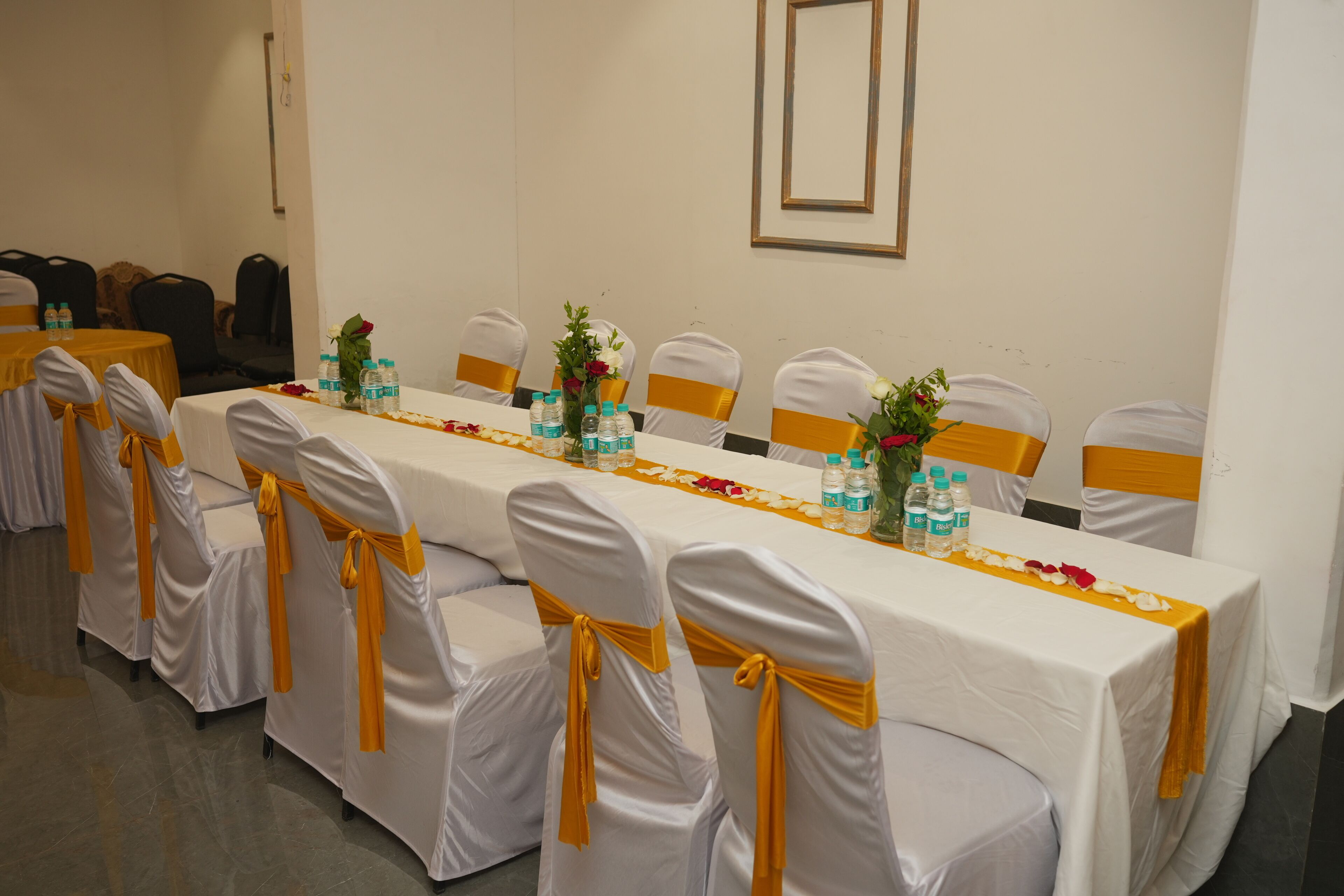 A conference room with a long table, chairs with yellow sashes, water bottles, and flower arrangements.