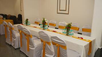 A conference room with a long table, chairs with yellow sashes, water bottles, and flower arrangements.