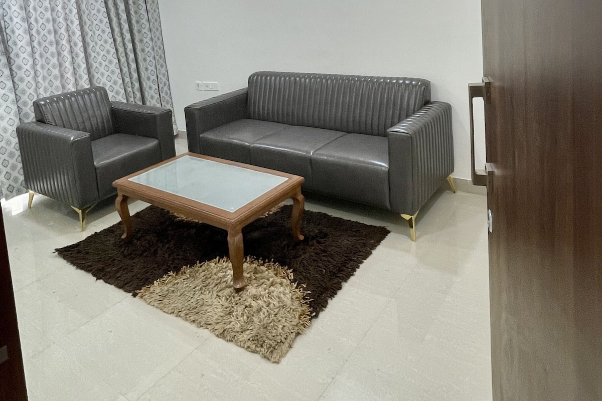Un salon avec un canapé gris, deux fauteuils, une table basse en bois et un tapis à motifs.