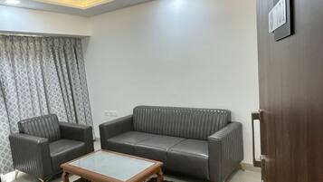 A living room with a grey sofa, two armchairs, a wooden coffee table, and a patterned rug.