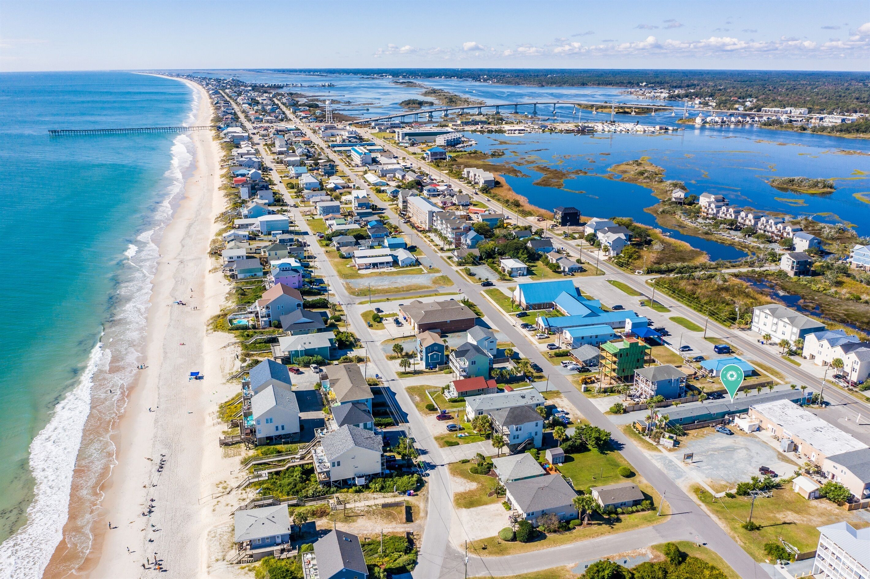 An aerial view of a coastal residential area with houses, a beach, and a bridge.