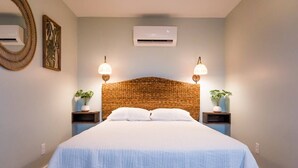 Una camera da letto con un letto grande, due comodini con lampade, una testiera in vimini e aria condizionata a muro.