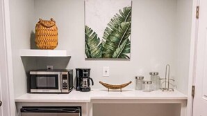 Una cucina compatta con forno a microonde, macchina del caffè e piccolo frigorifero.