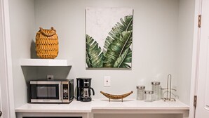 Eine kompakte Küche mit Mikrowelle, Kaffeemaschine und kleinem Kühlschrank. Auf der Arbeitsfläche befinden sich ein Korbwicker-Korb und eine gewebte Schüssel.
