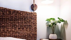 Un lit bien fait, agrémenté d’une tête de lit texturée, d’une lampe de chevet et d’une petite étagère sur laquelle est posée une plante.