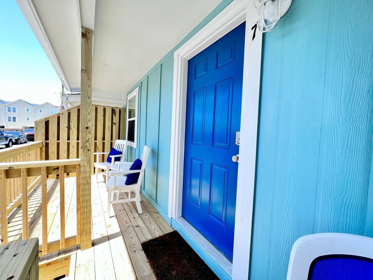 A wooden deck with a blue door, white walls, and a white chair.
