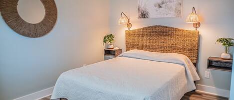 A bedroom with a large bed, two bedside tables, a round mirror, and a wall-mounted lamp.