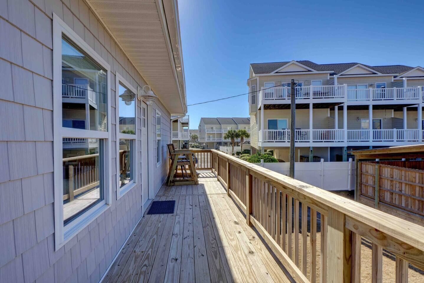 A wooden deck with a view of a beachfront building with multiple balconies and a clear sky.