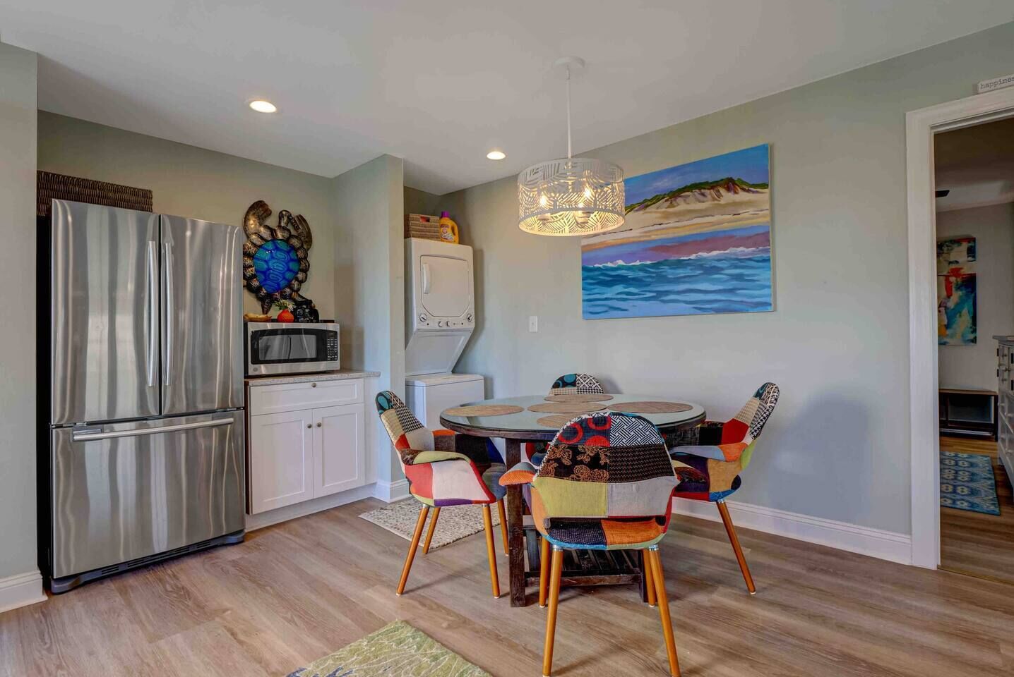A modern kitchen with a stainless steel refrigerator, a microwave, and a dining area with a round table and colorful chairs.