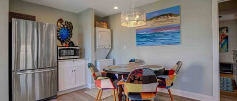 A modern kitchen with a stainless steel refrigerator, a microwave, and a dining area with a round table and colorful chairs.