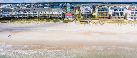 A coastal hotel with multiple buildings, a beach in the foreground, and a view of the ocean and sky.