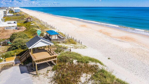 A beachside property with a wooden deck, a small building with a blue roof, and a fenced area.