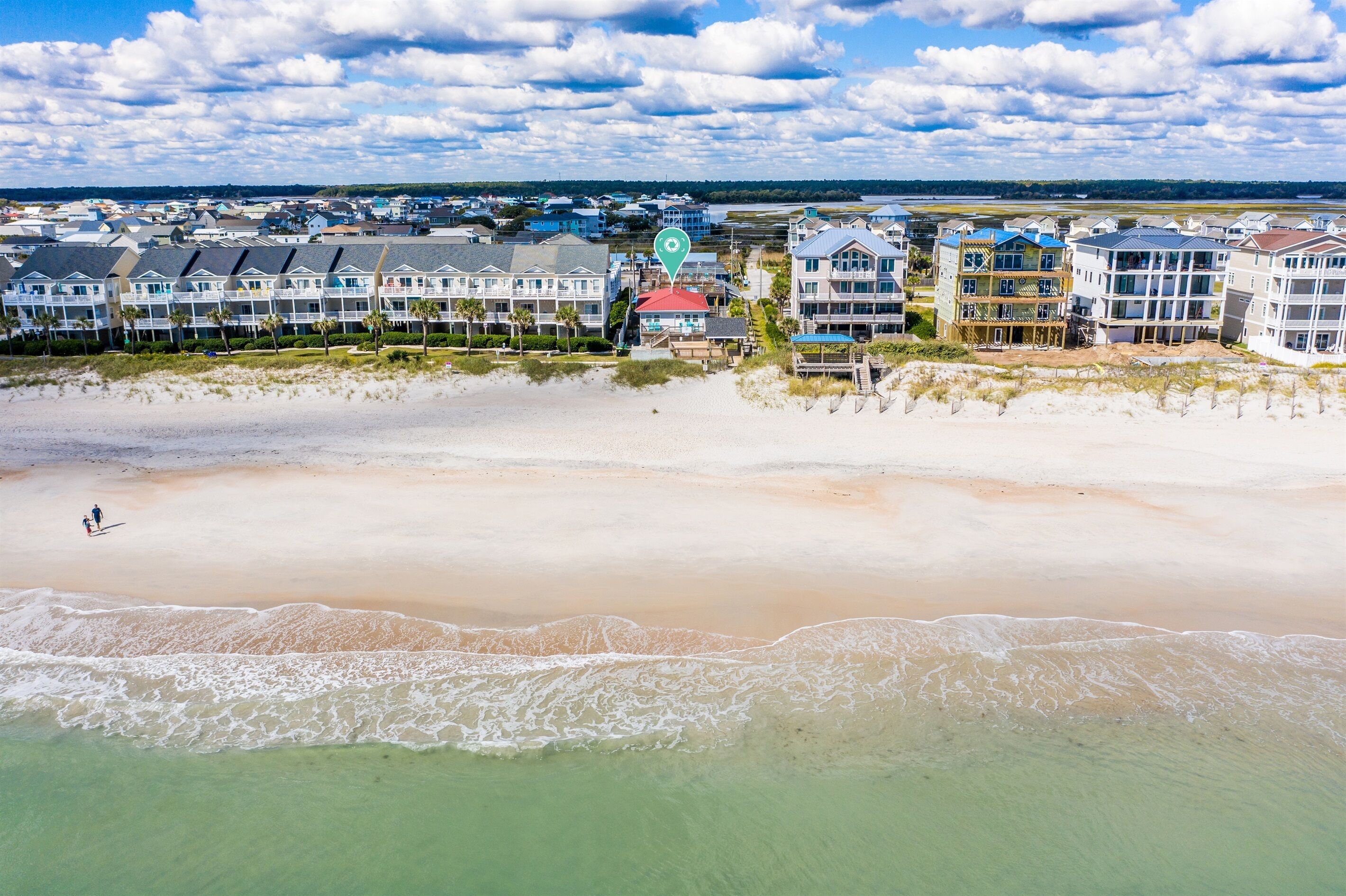 A coastal hotel with multiple buildings, a beach in the foreground, and a view of the ocean and sky.