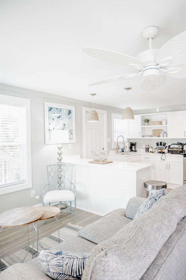A modern kitchen with white cabinetry, a central island, and a ceiling fan. - The Hideaway A- Beach - Dog Friendly - Playset - Bikes - Fenced in Yard (Surf City)