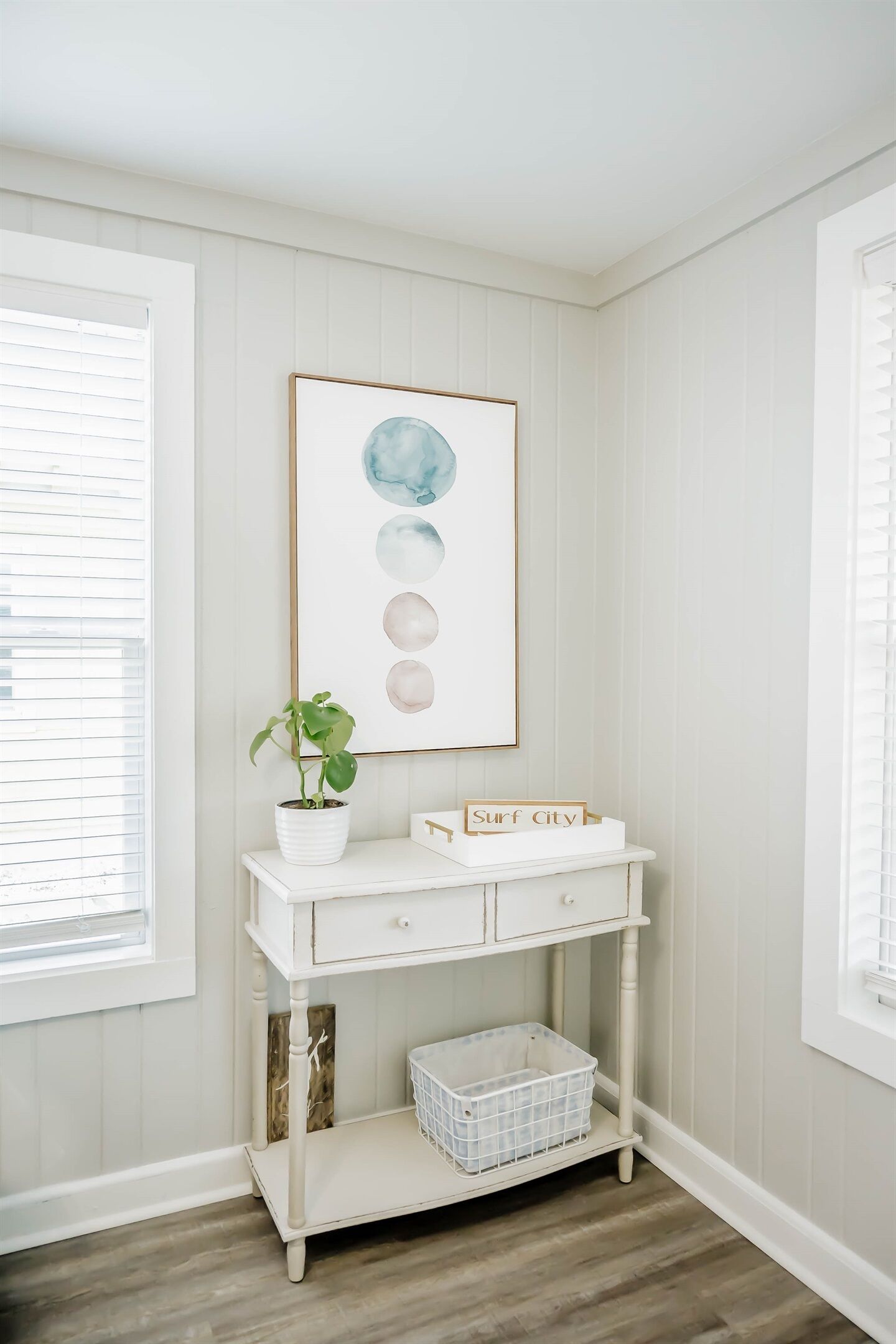 A white console table with a potted plant, a framed artwork, and a sign that reads "Surf City".