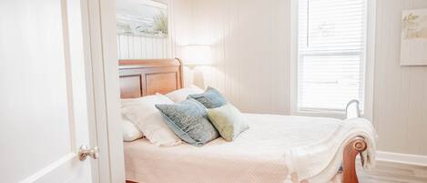 A bedroom with a wooden bed frame, white bedding, and a window with blinds.