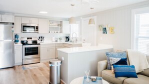 A modern kitchen with white cabinets, stainless steel appliances, and a central island. - The Hideaway B- Beach - Dog Friendly - Playground - Bikes - Fenced in Yard (Surf City)