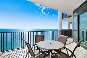 A balcony with a round table and four chairs, overlooking a clear blue sea. - The Oasis 2505 | Spacious, Lazy River, Poolside Grill, New Splash Pad, Pool with Slide! (Orange Beach)