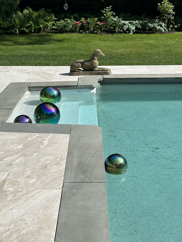 A swimming pool with three iridescent spheres and a stone sculpture.
