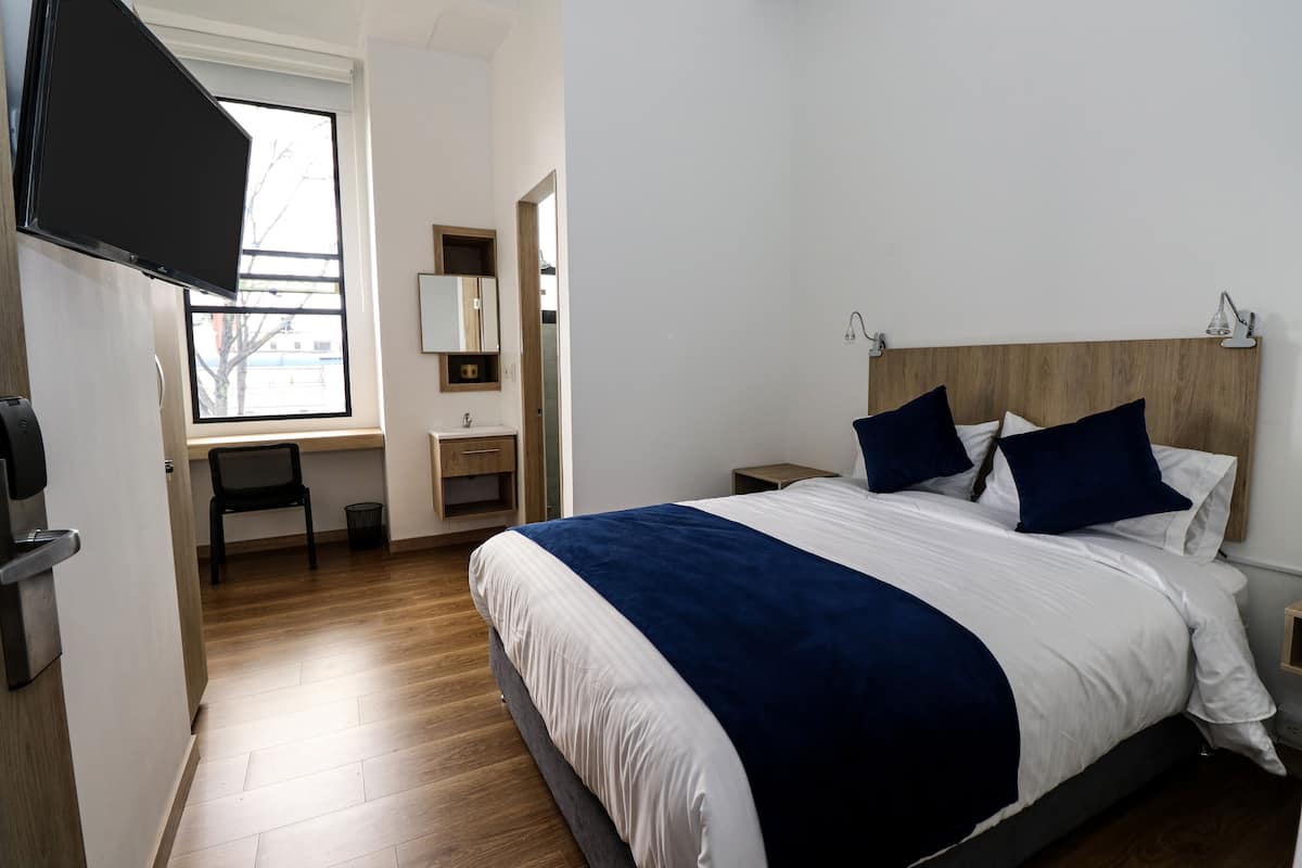 A bedroom with a large bed, a desk, a mirror, and a window.