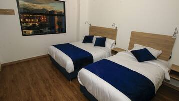 A hotel room with two beds, wooden flooring, and a large window with a city view.
