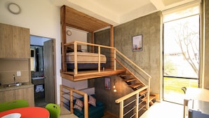 En kompakt lejlighed med et soveværelse på loftet, et køkken og et spiseområde.