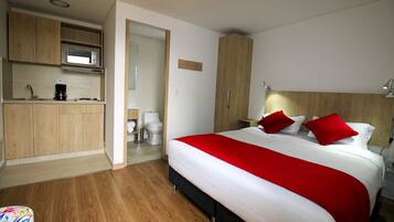 A hotel room with a bed, a wooden wardrobe, a kitchenette, and a bathroom.