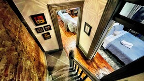 Escadaria que leva a um quarto com uma cama, um criado-mudo e uma luminária na parede.