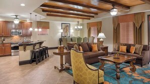 A spacious living area with a large sofa, a coffee table, and a patterned rug. There is a kitchen area with wooden cabinets and a microwave. - 4 Bedroom Presidential Suite inside Disney Property @ Wyndham's Bonnet Creek (Lake Buena Vista)