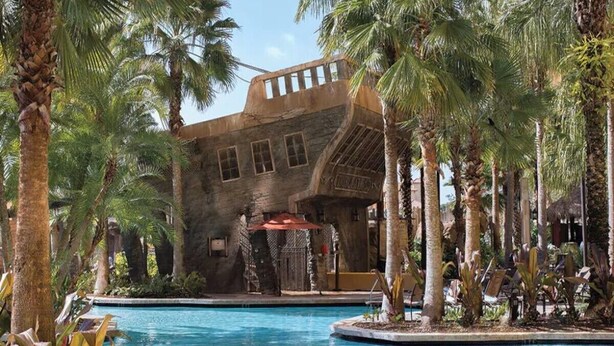 A pool area with palm trees and a stone building. - 4 Bedroom Presidential Suite inside Disney Property @ Wyndham's Bonnet Creek (Lake Buena Vista)